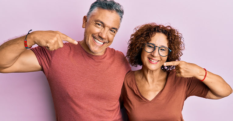 man and woman smiling pointing at teeth